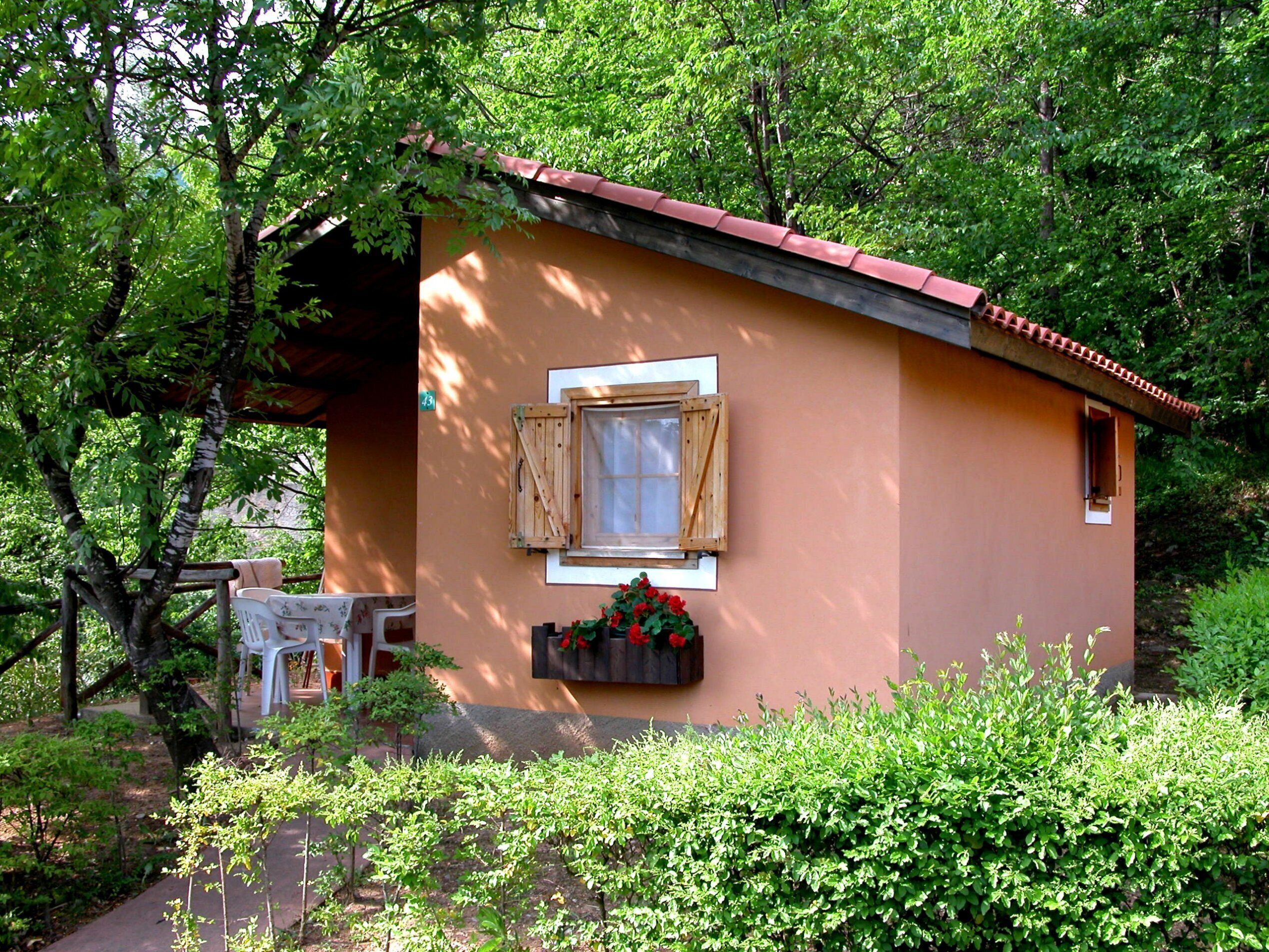 A small, single-story building with a red roof, a window with wooden shutters, and a planter box with red flowers.