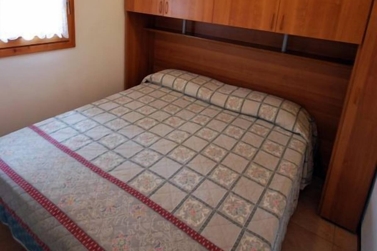 A bedroom with a bed, wooden headboard, and a window with a curtain.