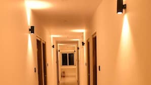 A hallway with marble flooring, light-colored walls, and wall-mounted light fixtures. - Hotel Waanderers Howff (Port Blair)
