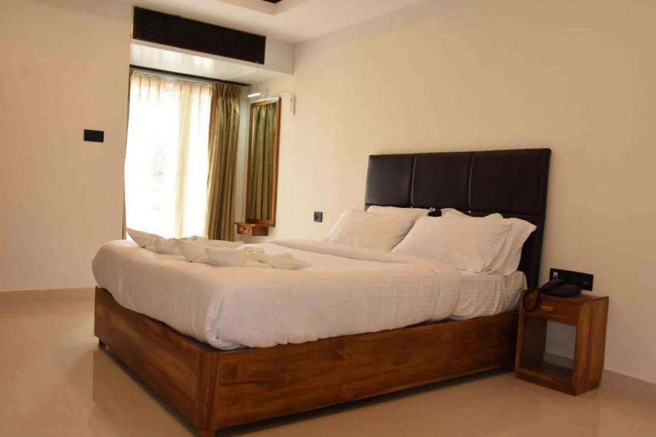 A modern bedroom with a wooden bed frame, white bedding, and a nightstand with a lamp.