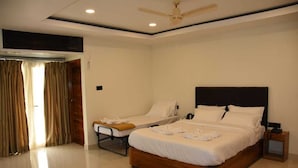 A hotel room with a large bed, a smaller bed, a bedside table, a nightstand, a ceiling fan, and a window with curtains. - Hotel Waanderers Howff (Port Blair)