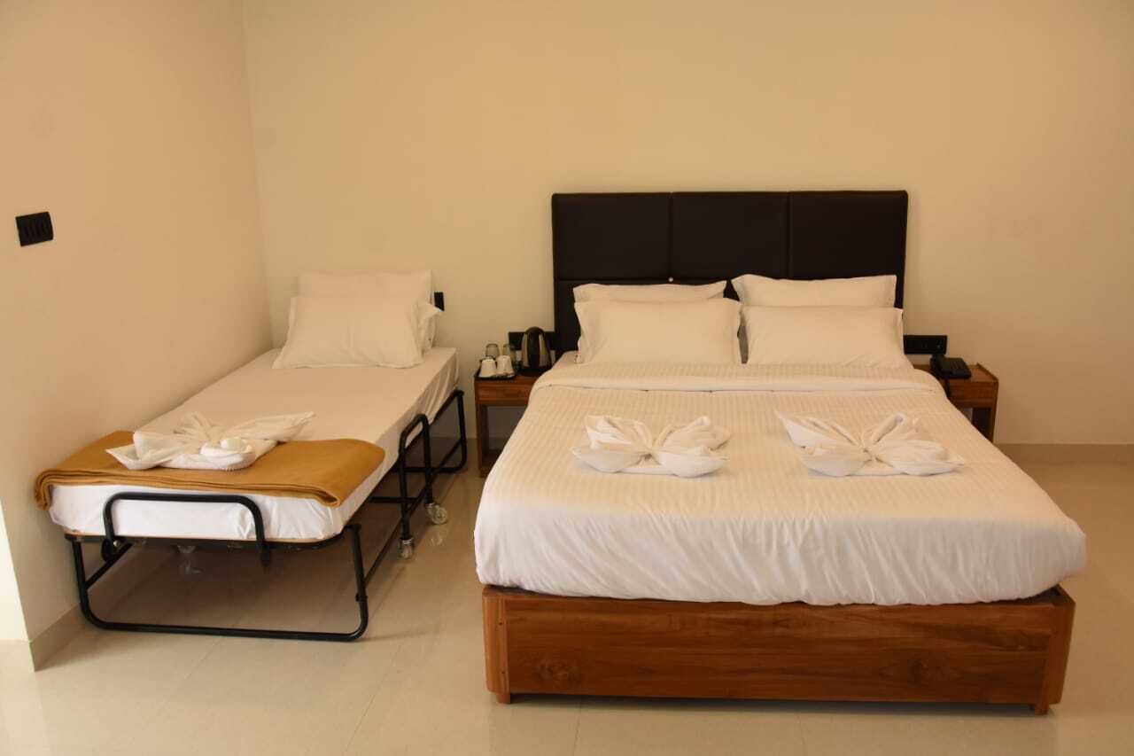 A hotel room with two beds, one with a wooden frame and the other with a metal frame, both with white linens and towels.