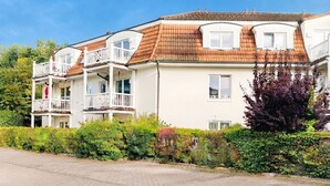 A multi-story residential building with a tiled roof, balconies, and a paved driveway.