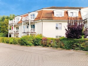 A multi-story residential building with a tiled roof, balconies, and a paved driveway.