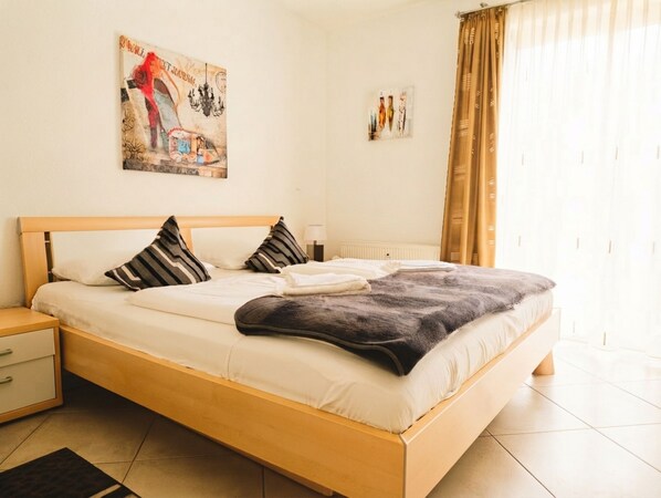 A neatly made bed with pillows and a blanket, a bedside table with a lamp, and a painting on the wall.