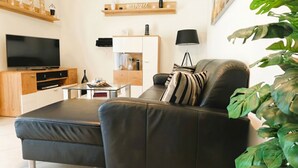 A modern living room with a leather sofa, a flat-screen TV, a wooden cabinet, and a small dining table.
