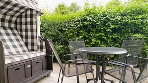 En patio med en skaktern udendørssofa, et rundt metalbord og fire stole med mesh-ryg.