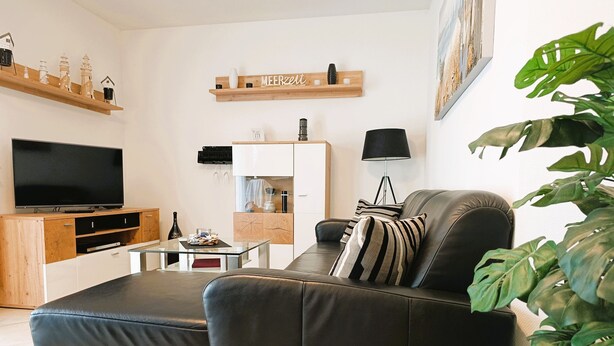 En moderne stue med en lædersofa, et fladskærms-tv, et sofabord og et køkkenområde med et køleskab og en mikrobølgeovn.