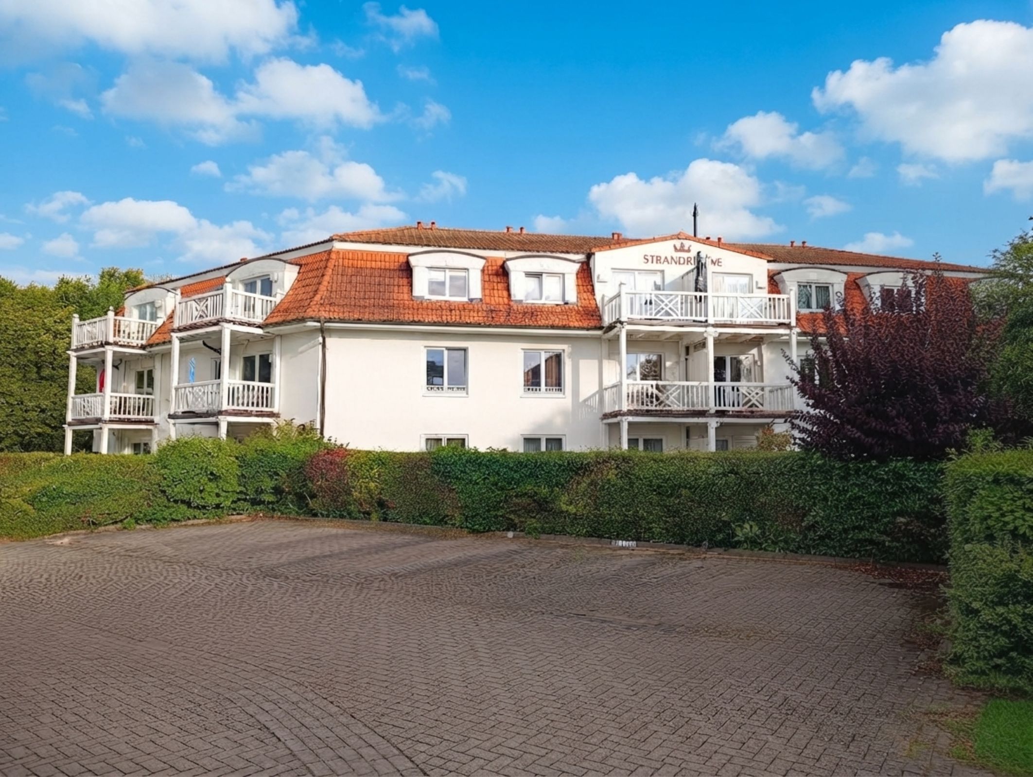 A multi-story hotel with a red-tiled roof, balconies, and a paved driveway.