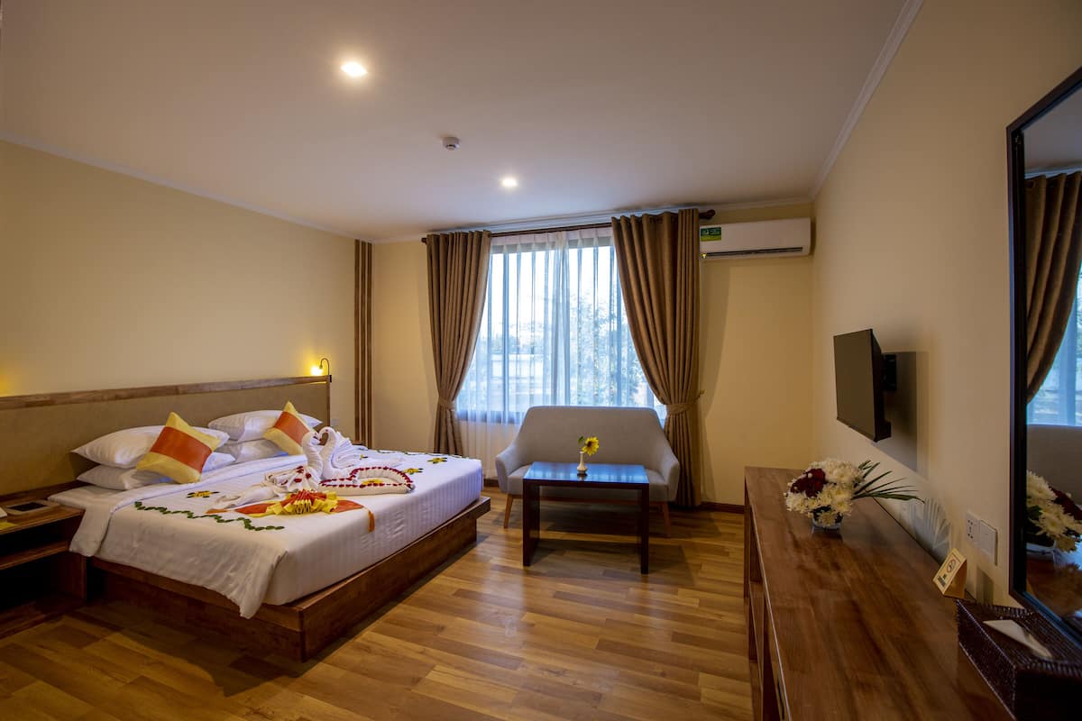 A hotel room with a bed, a sofa, a desk, and a large window with curtains.