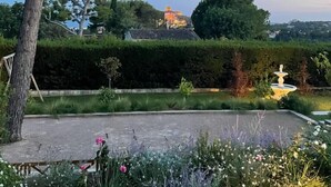 Un jardín ajardinado con una fuente, setos podados y diversas plantas.