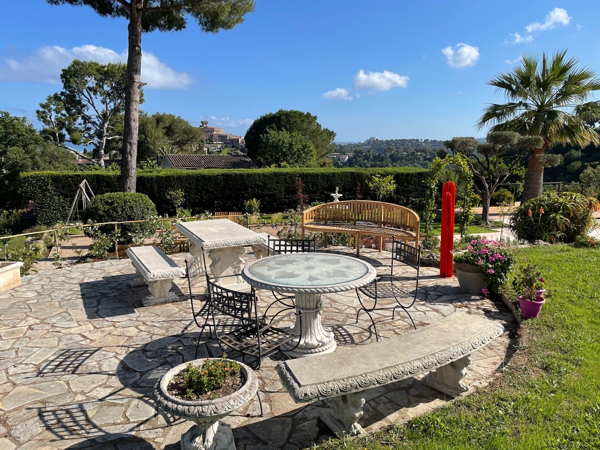 A stone patio with a round table and chairs, a bench, and a decorative fountain.