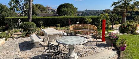 A stone patio with a round table and chairs, a bench, and a decorative fountain.