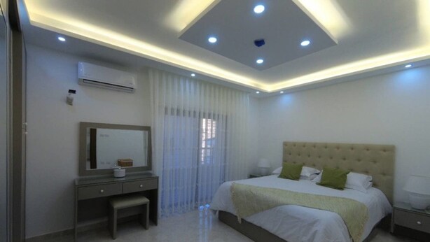 A modern bedroom with a large bed, a bedside table, a mirror, and an air conditioning unit on the wall. - Amazing one Bedroom Apartment in Amman, Elwebdah 2 (Amman)