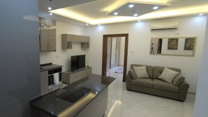 A modern living room with a kitchen area, a sofa, and a TV. - Amazing one Bedroom Apartment in Amman,elwebdah 1 (Amman)