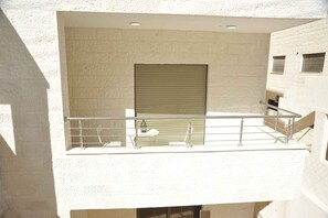A balcony with a metal railing, a closed shutter, and a small table with chairs. - Amazing one Bedroom Apartment in Amman,elwebdah 6 (Amman)
