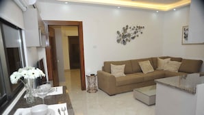 A modern living room with a beige sofa, a coffee table, and a dining area with a marble countertop and a vase of white flowers. - Amazing one Bedroom Apartment in Amman,elwebdah 6 (Amman)