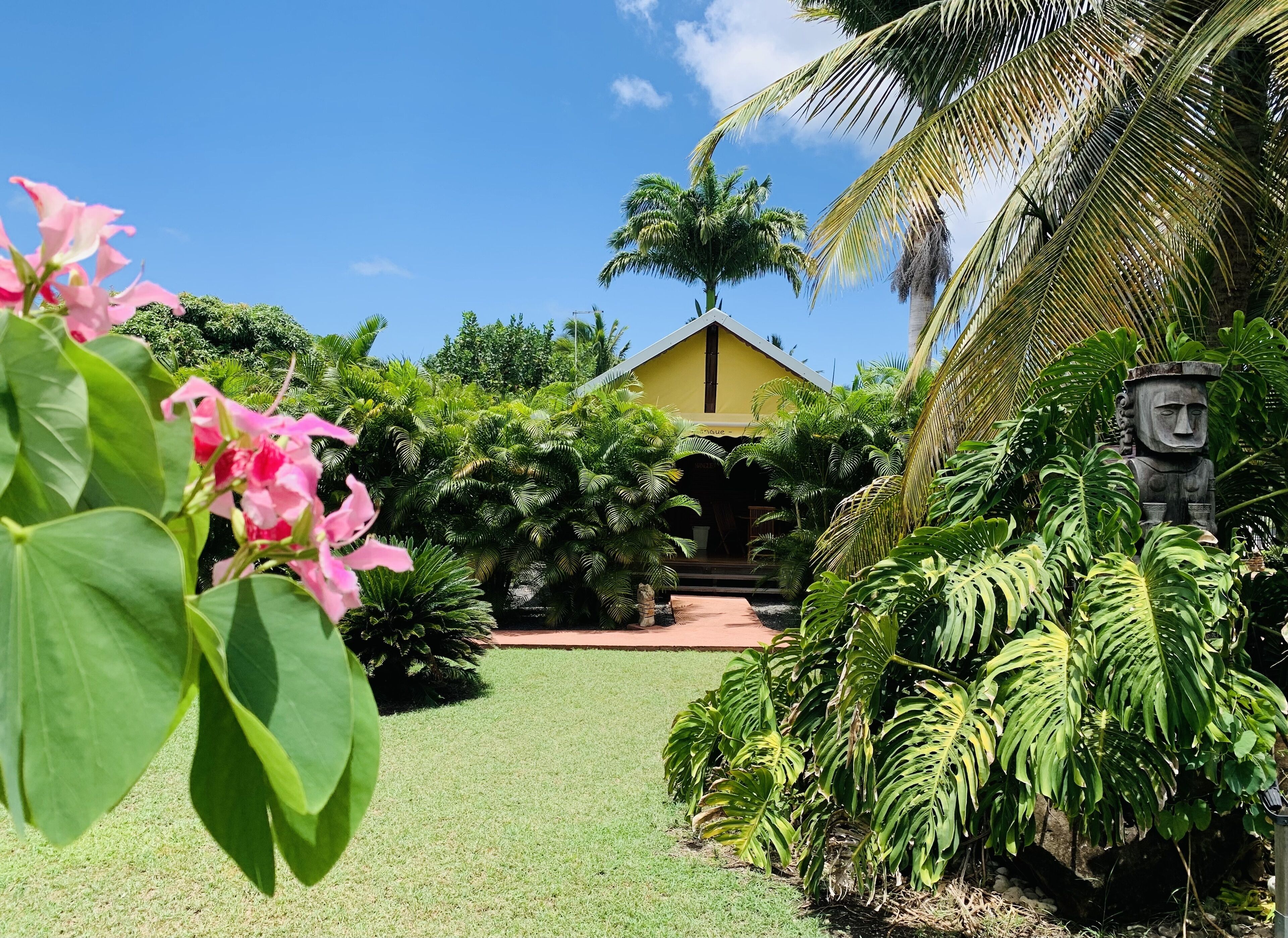 A tropical garden with a yellow building, lush greenery, and a statue.