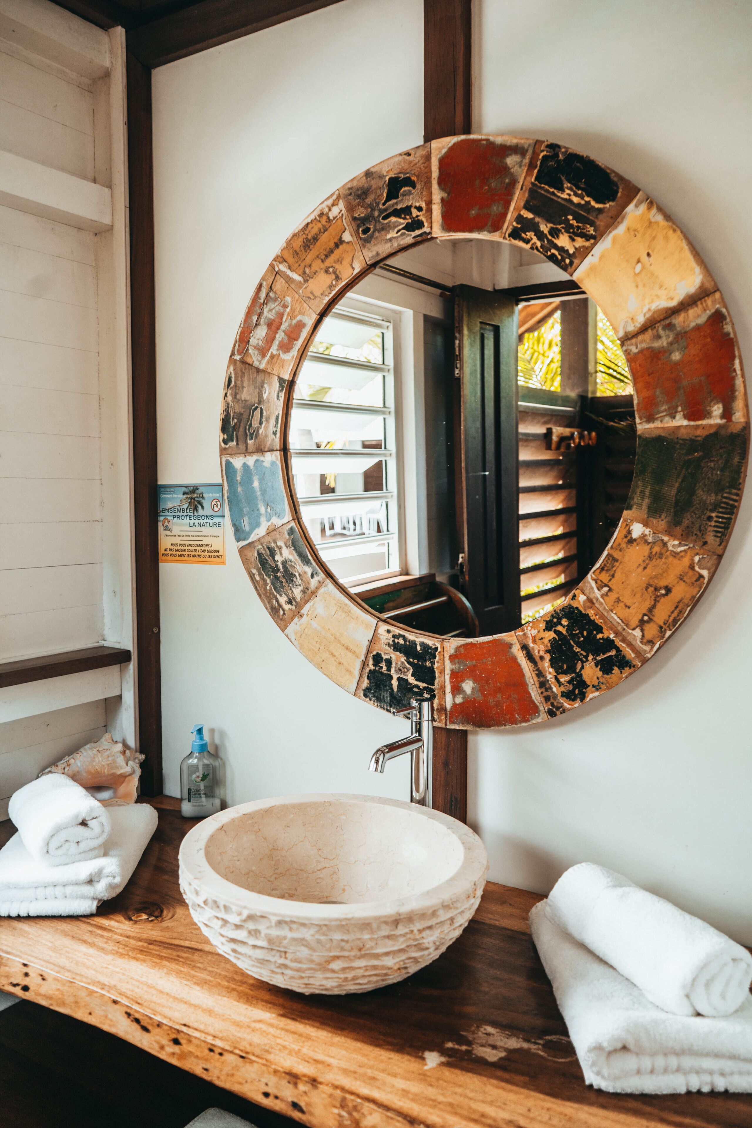 A bathroom with a round mirror, wooden countertop, and a bowl sink.