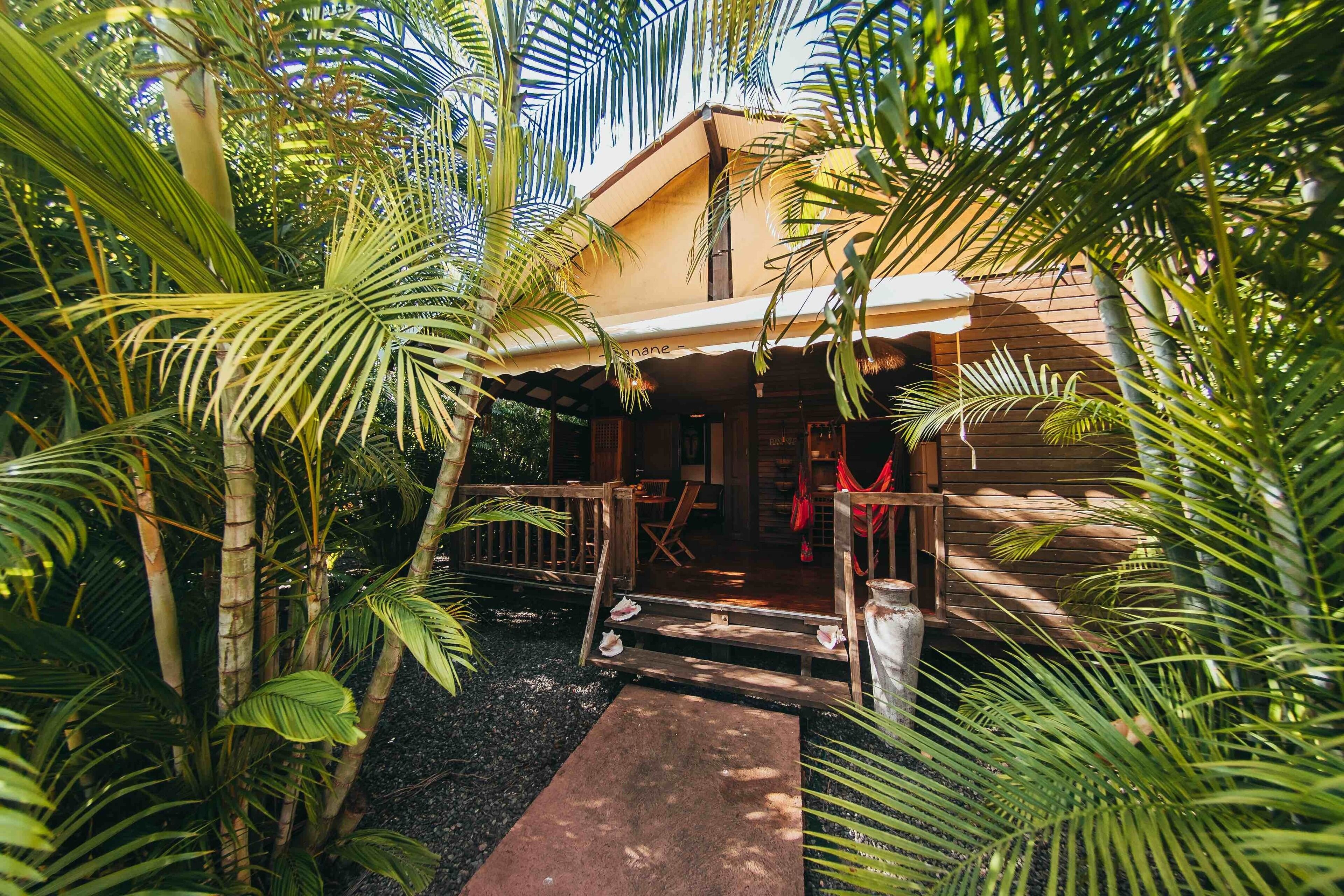 Ein Holzhaus mit Veranda, umgeben von tropischen Pflanzen.