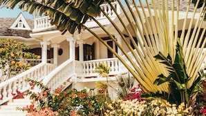 A white colonial-style building with a white staircase leading to a balcony, surrounded by tropical plants and colorful flowers. - Domaine Saint-François (Saint-François)