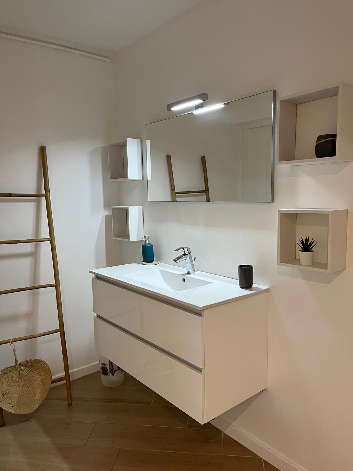 Un baño moderno con un tocador blanco, un espejo grande y estantes integrados.