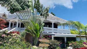 A colonial-style house with a white porch and a garden with colorful flowers and tropical plants. - Domaine Saint-François (Saint-François)