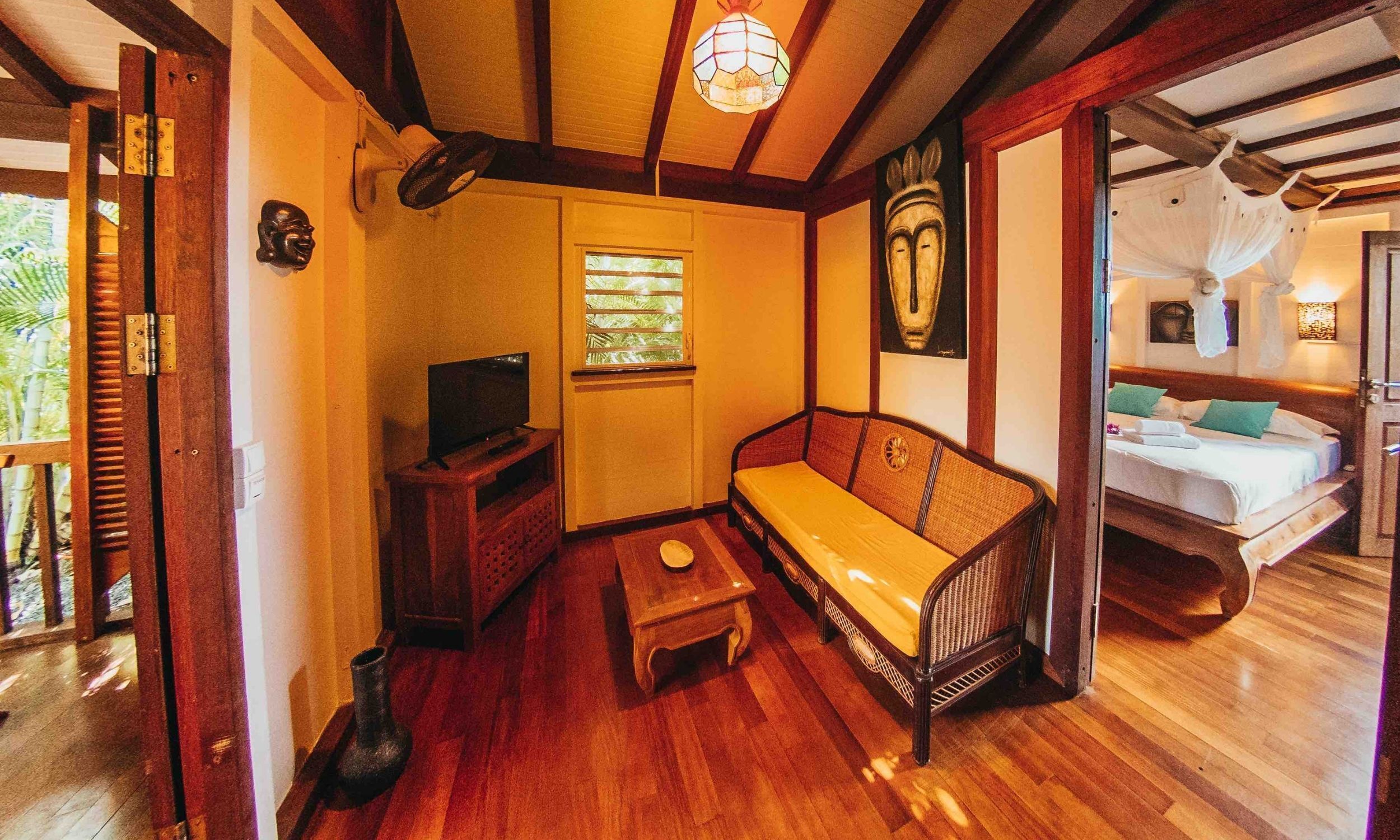 A cozy room with a wooden floor, a sofa, a TV, a small table, and a window with blinds.