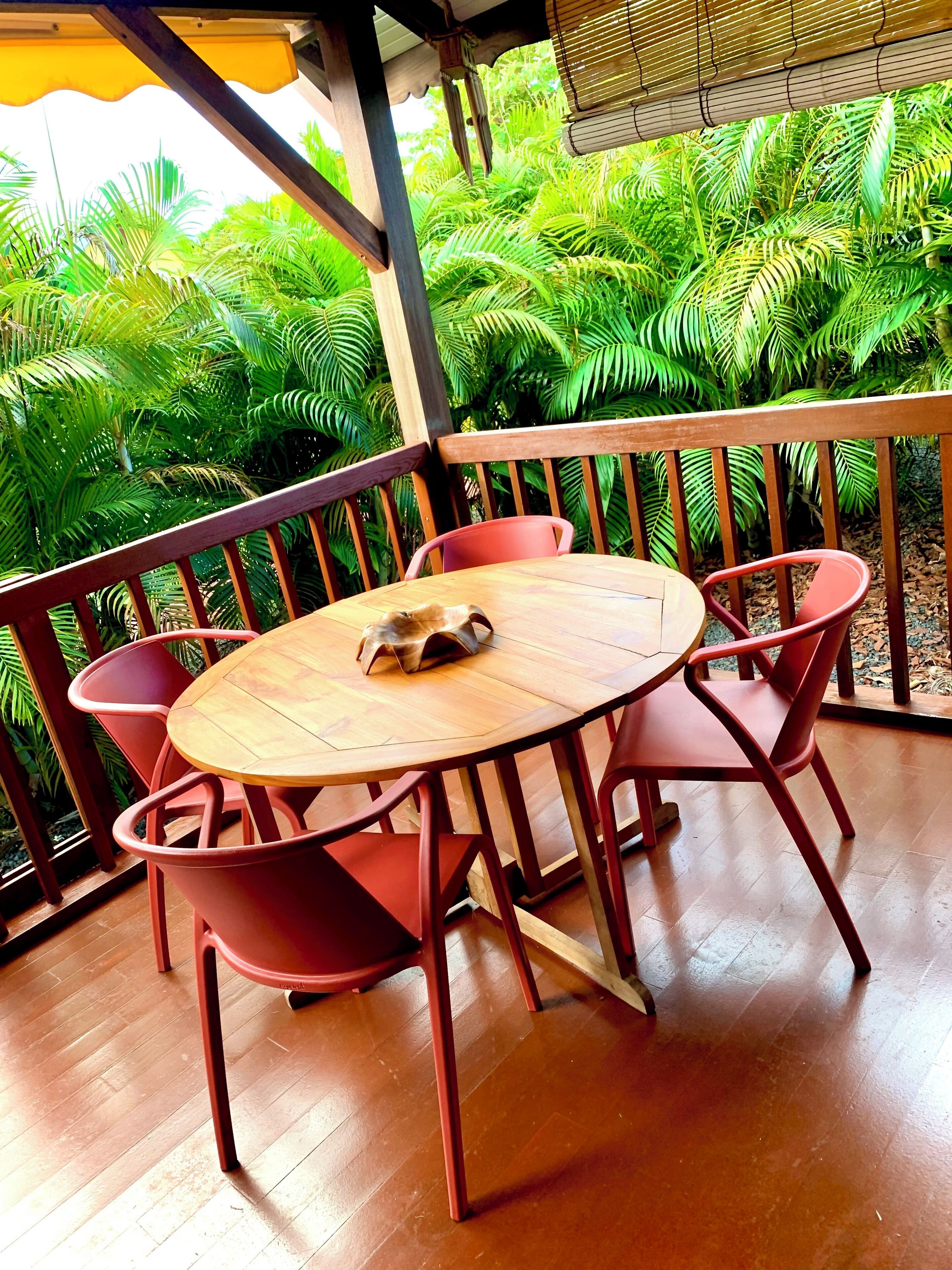 A wooden table and chairs on a balcony with a view of lush green foliage.