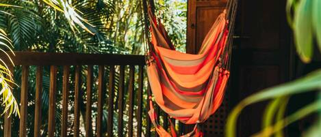A hammock hanging on a wooden deck with a view of lush greenery and a wooden fence.