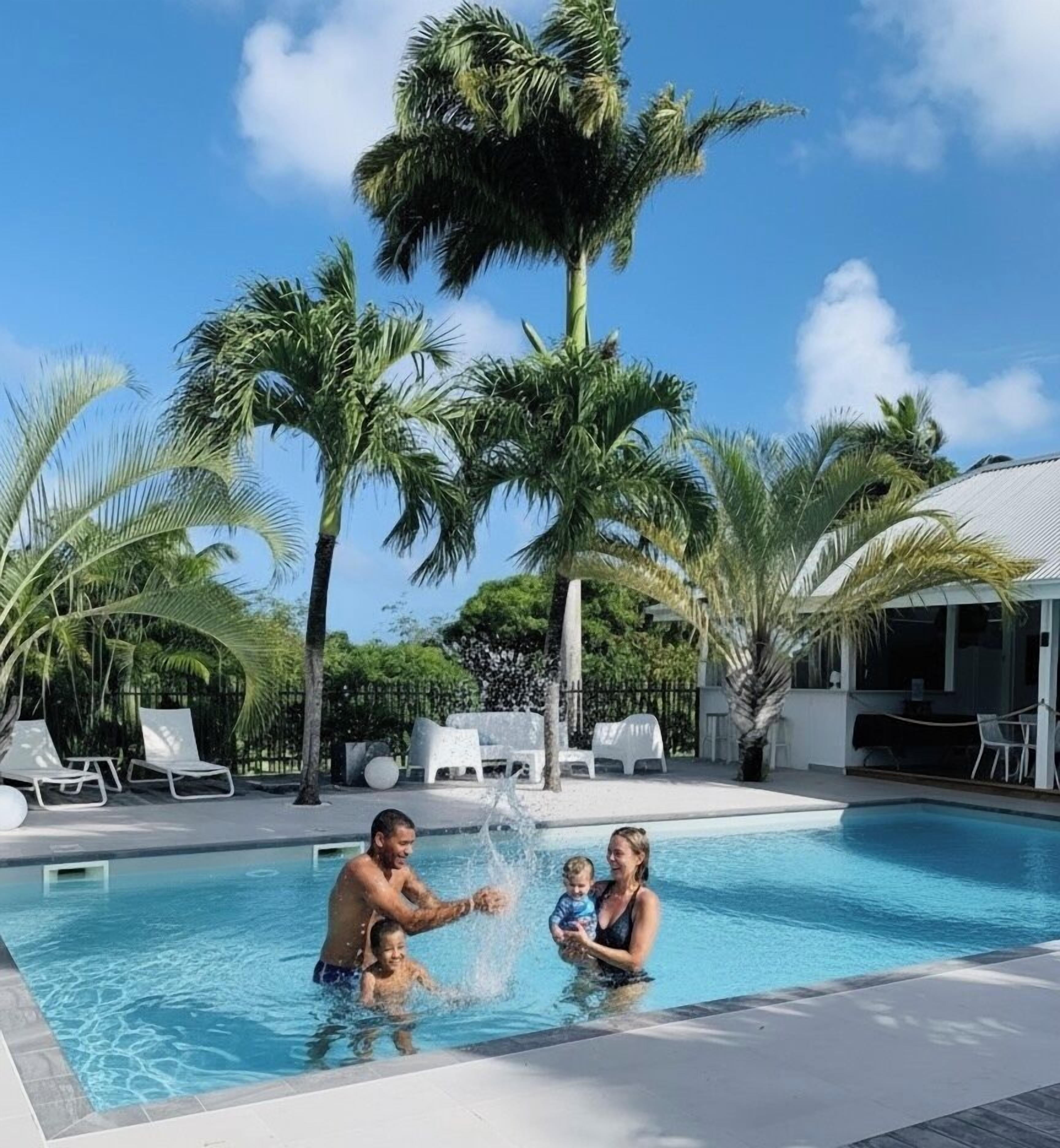 A swimming pool with palm trees, lounge chairs, and a covered area.