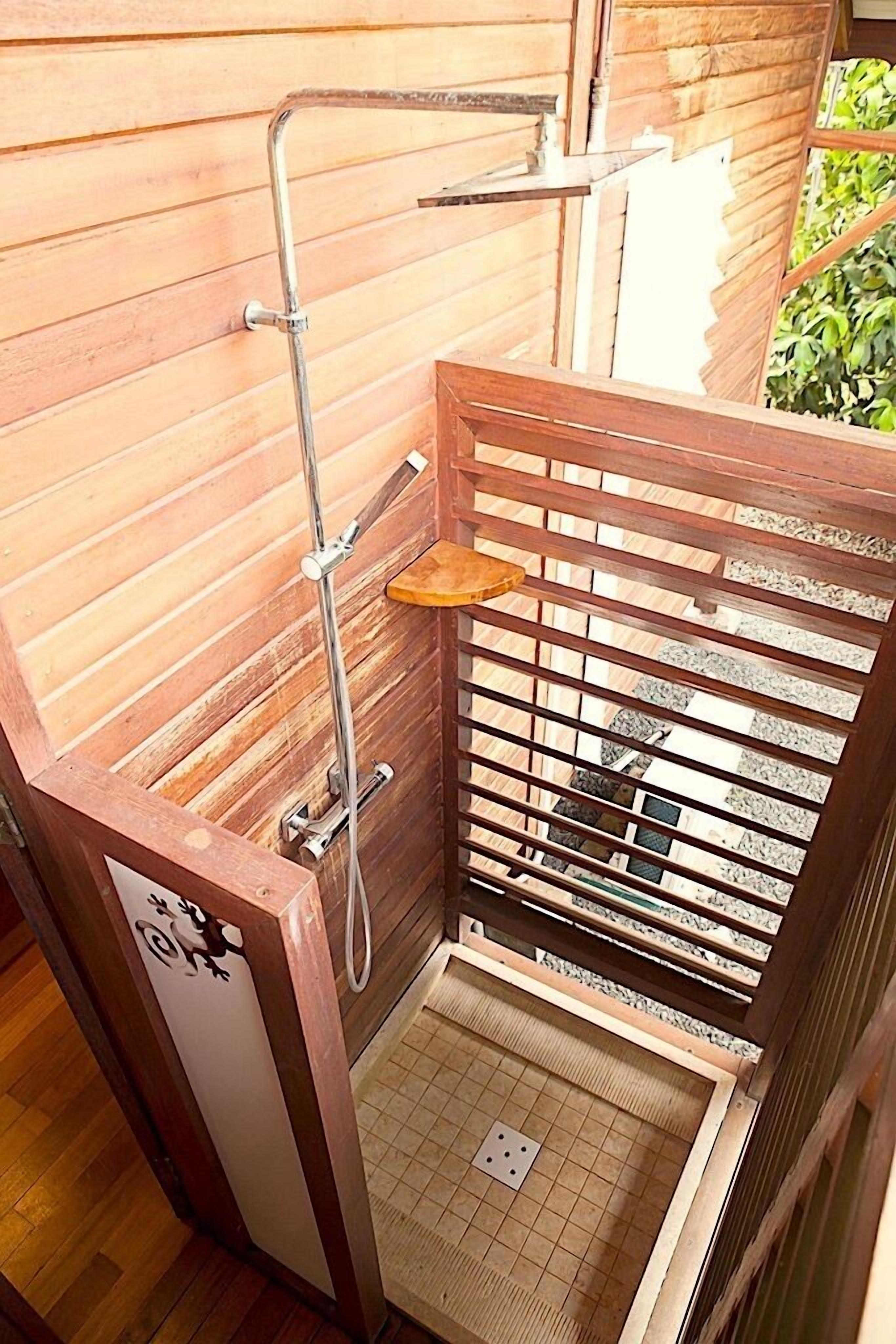 Un espace de douche en bois, doté d’un pommeau de douche en métal et d’une petite étagère en bois.