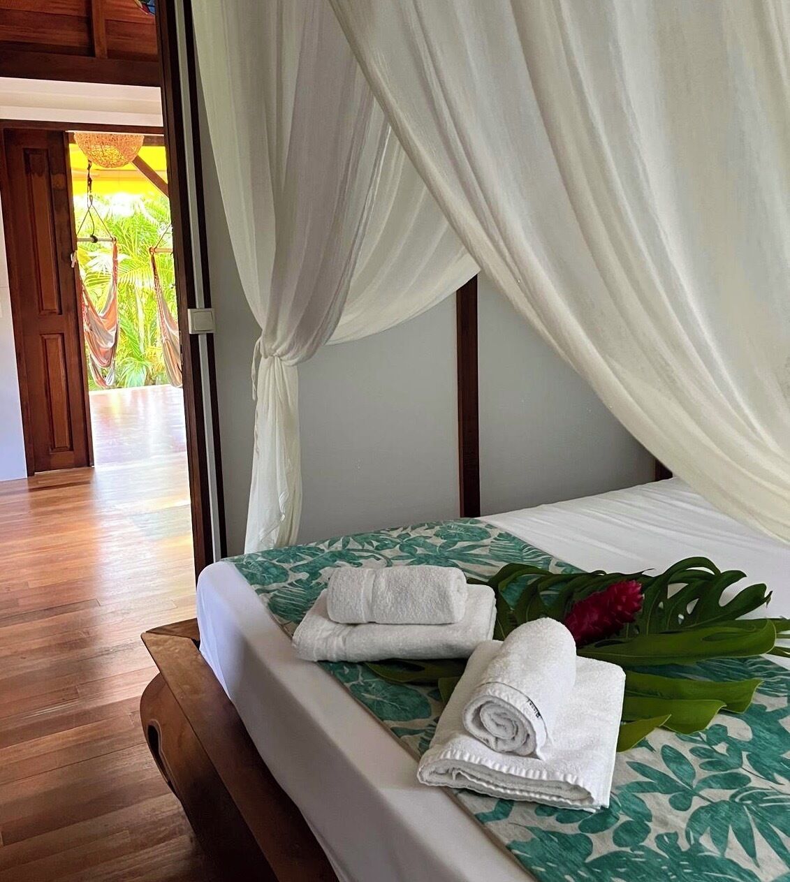 Habitación de hotel con cama, cortinas blancas y vista a una puerta de madera que da al exterior.