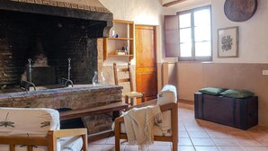 Una habitación rústica con chimenea de piedra, muebles de madera y una ventana con persianas.