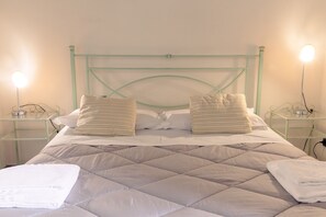 A neatly made bed with a quilted headboard, two bedside tables with lamps, and a stack of folded towels on each side. - La Torre Rasa (Castelfiorentino)