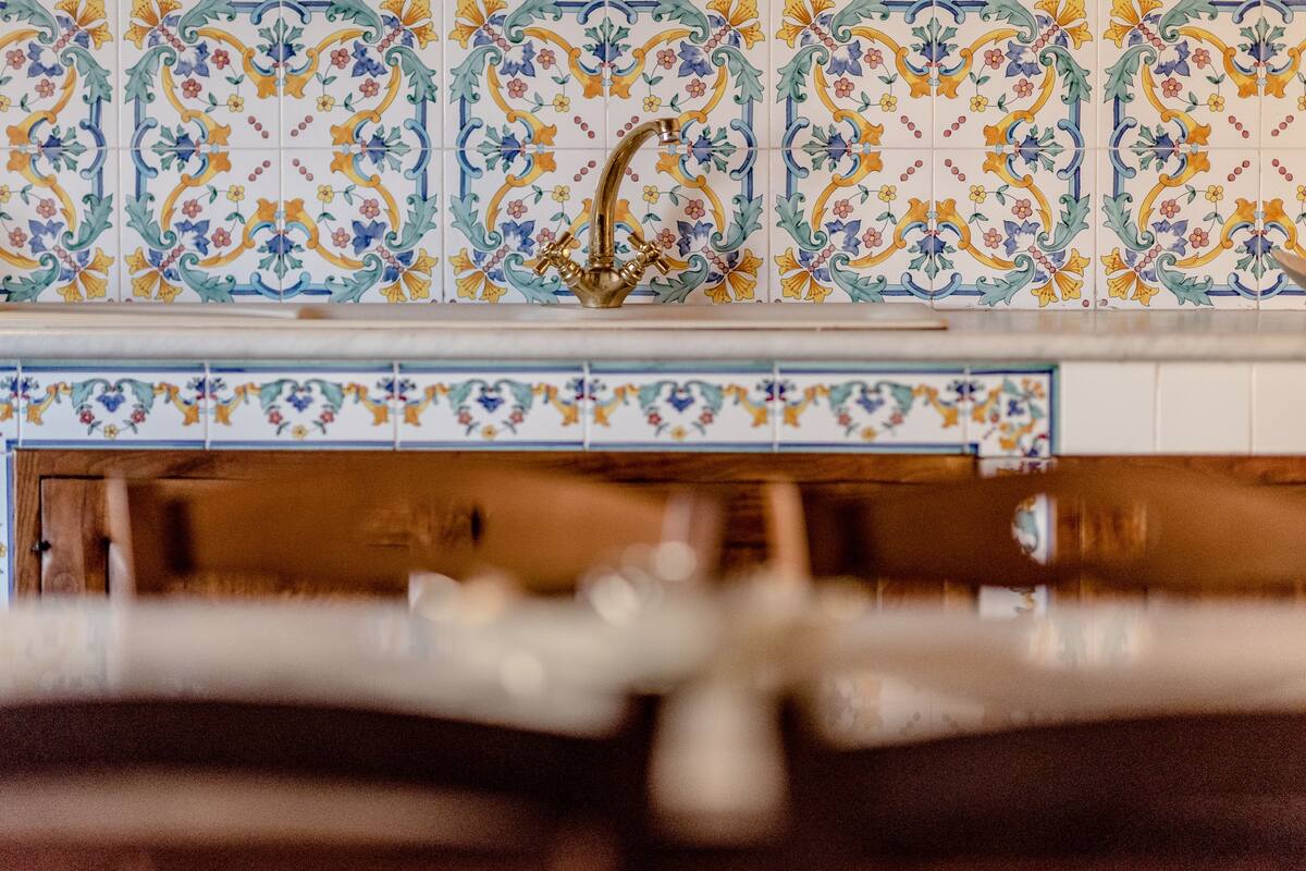 A kitchen with a tiled backsplash featuring a floral pattern and a gold faucet.