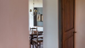Un acceso a un comedor con una mesa y sillas de madera, una lámpara colgante y un toallero en la pared.