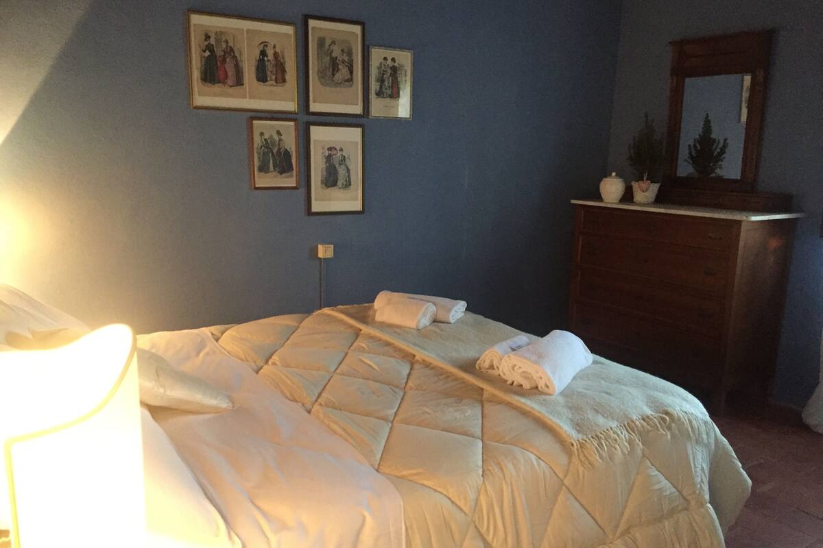 A neatly made bed with a quilted blanket, a wooden dresser with a mirror, and framed pictures on the wall.