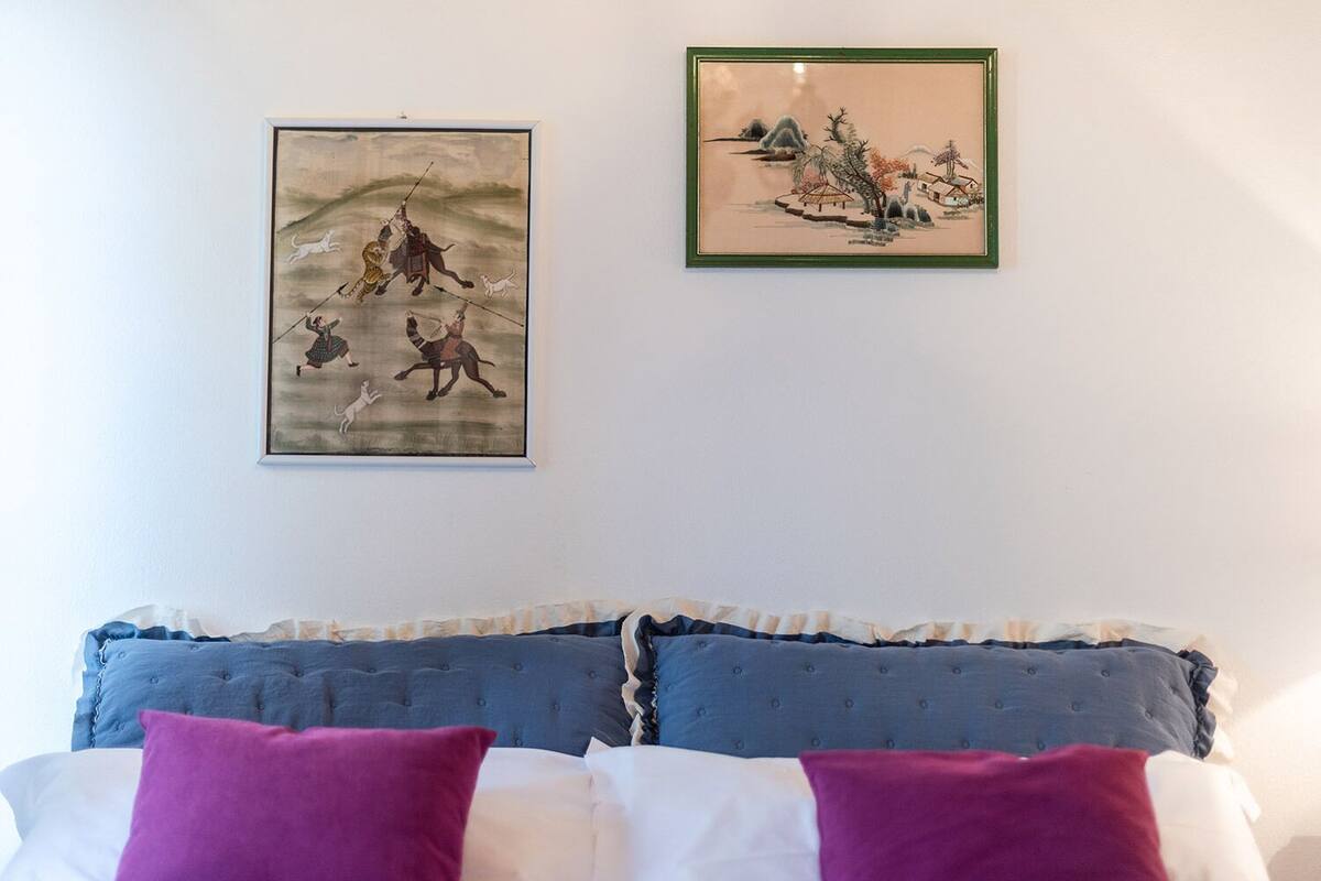 A bedroom with a bed, pillows, and two framed artworks on the wall.