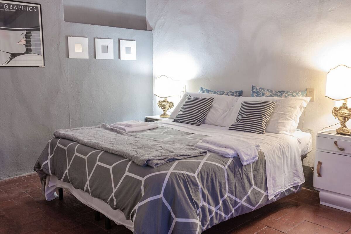 A neatly made bed with a geometric patterned bedspread, two bedside tables with lamps, and a wall with framed pictures.