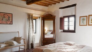 Un dormitorio con cama, banca de madera, espejo y ventana.
