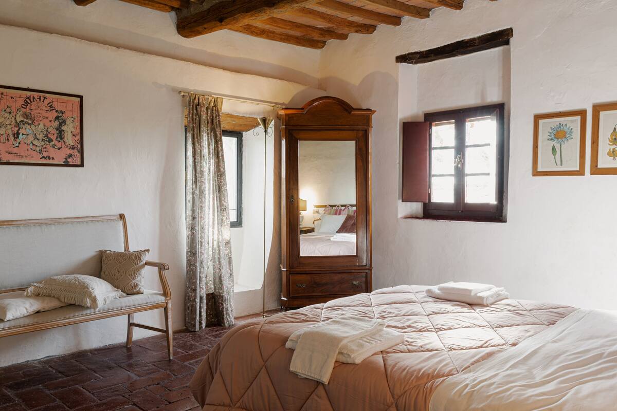 A bedroom with a bed, a wooden bench, a mirror, and a window.