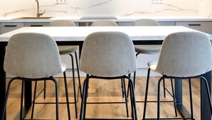 Una cocina moderna con encimera de mármol, tres taburetes de bar e iluminación colgante.
