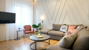 Una sala de estar moderna con un sofá, un sillón, una mesa de centro redonda y un televisor montado en la pared.