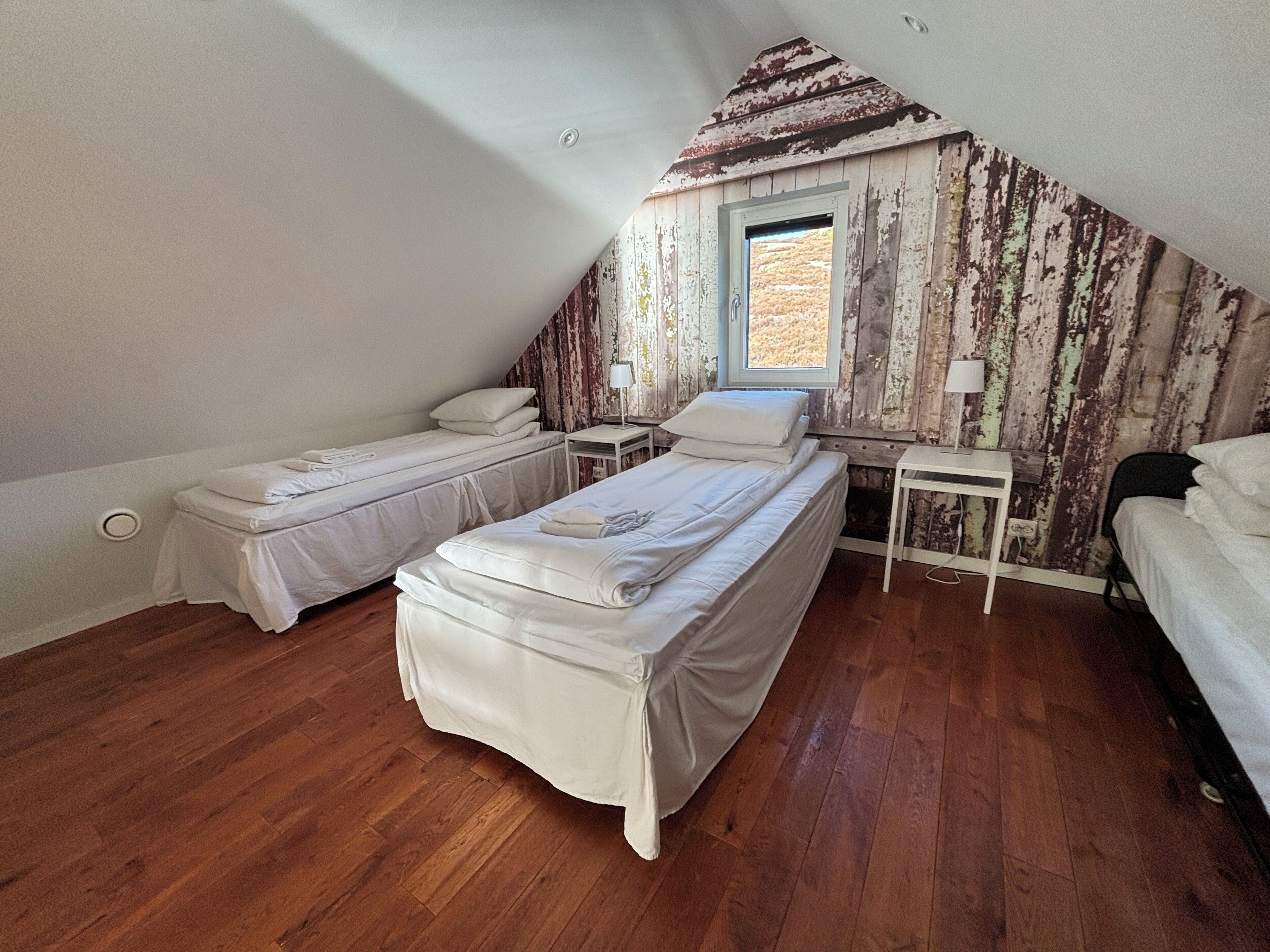 Un dormitorio cálido y acogedor en el ático, con dos camas individuales, una ventana y un muro de madera rústica.