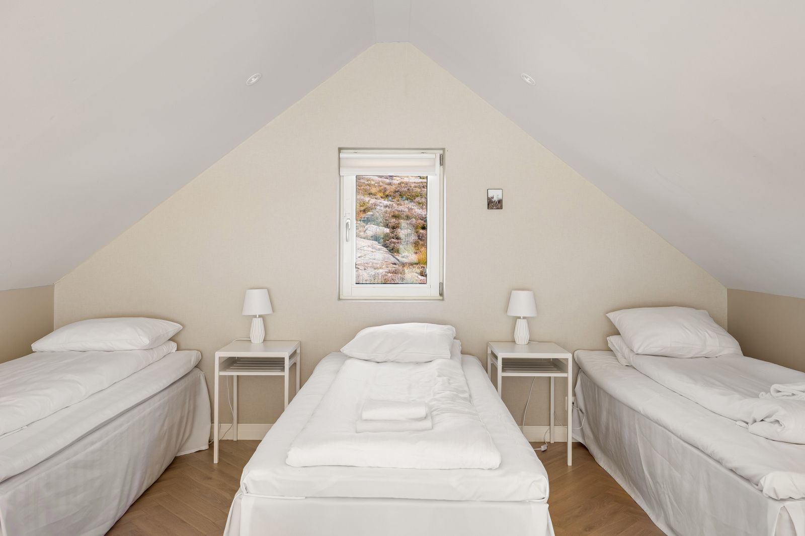 Habitación con dos camas individuales, una cama en el centro y ventana con vista a un paisaje rocoso.