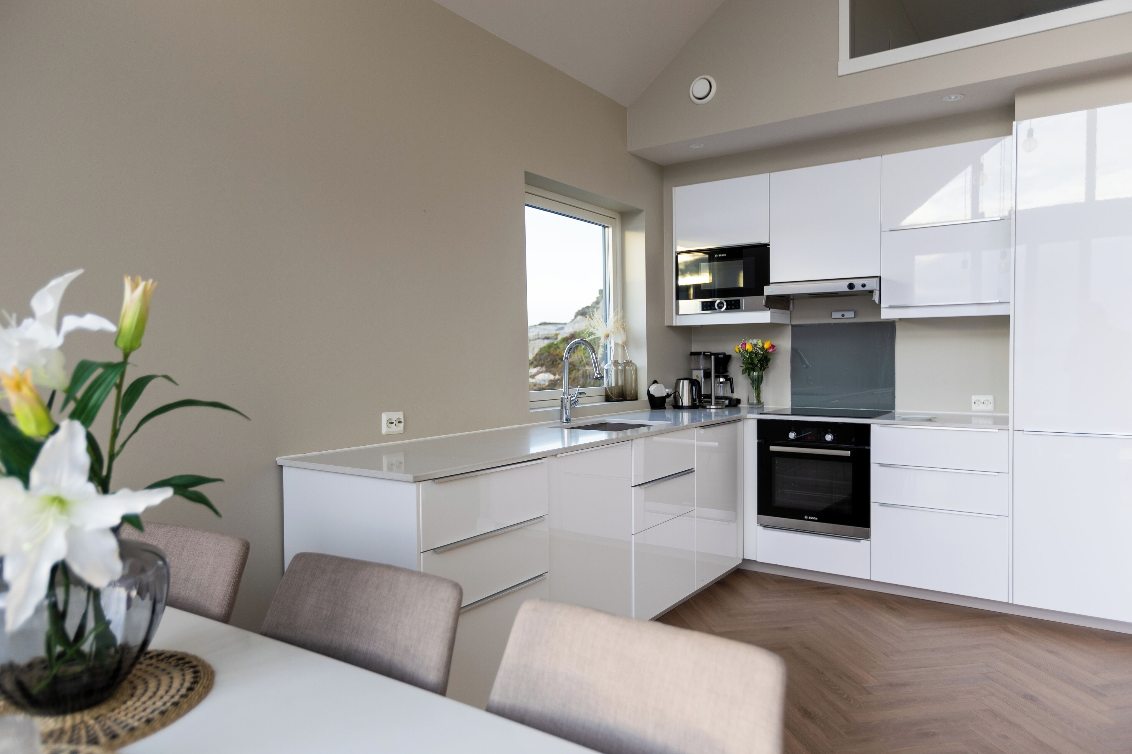 A modern kitchen with white cabinets, a built-in oven, and a window overlooking a scenic view.