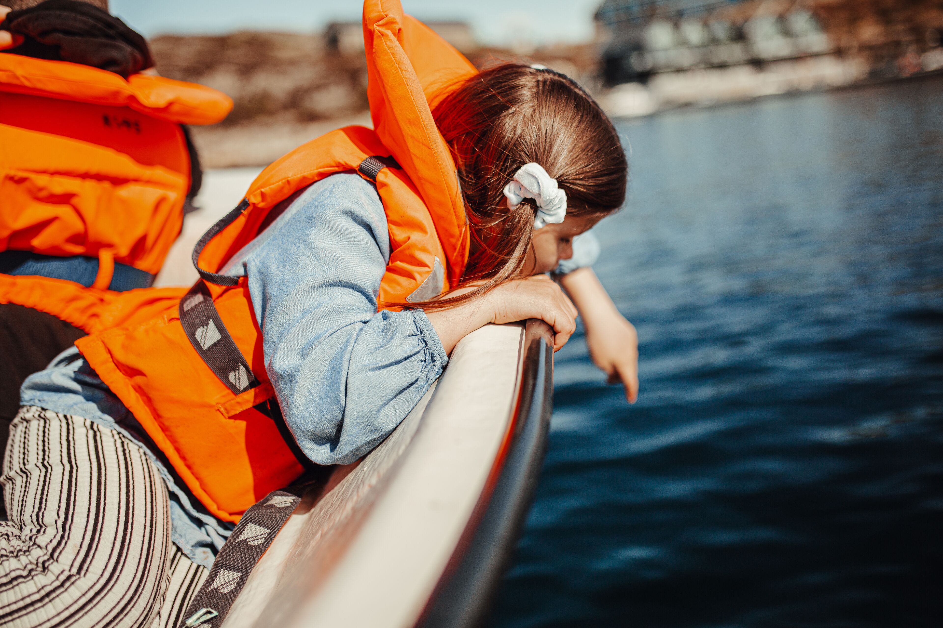 Een persoon in een oranje redvest leunt tegen de rand van een boot.