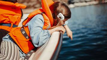 Een persoon in een oranje redvest leunt tegen de rand van een boot.