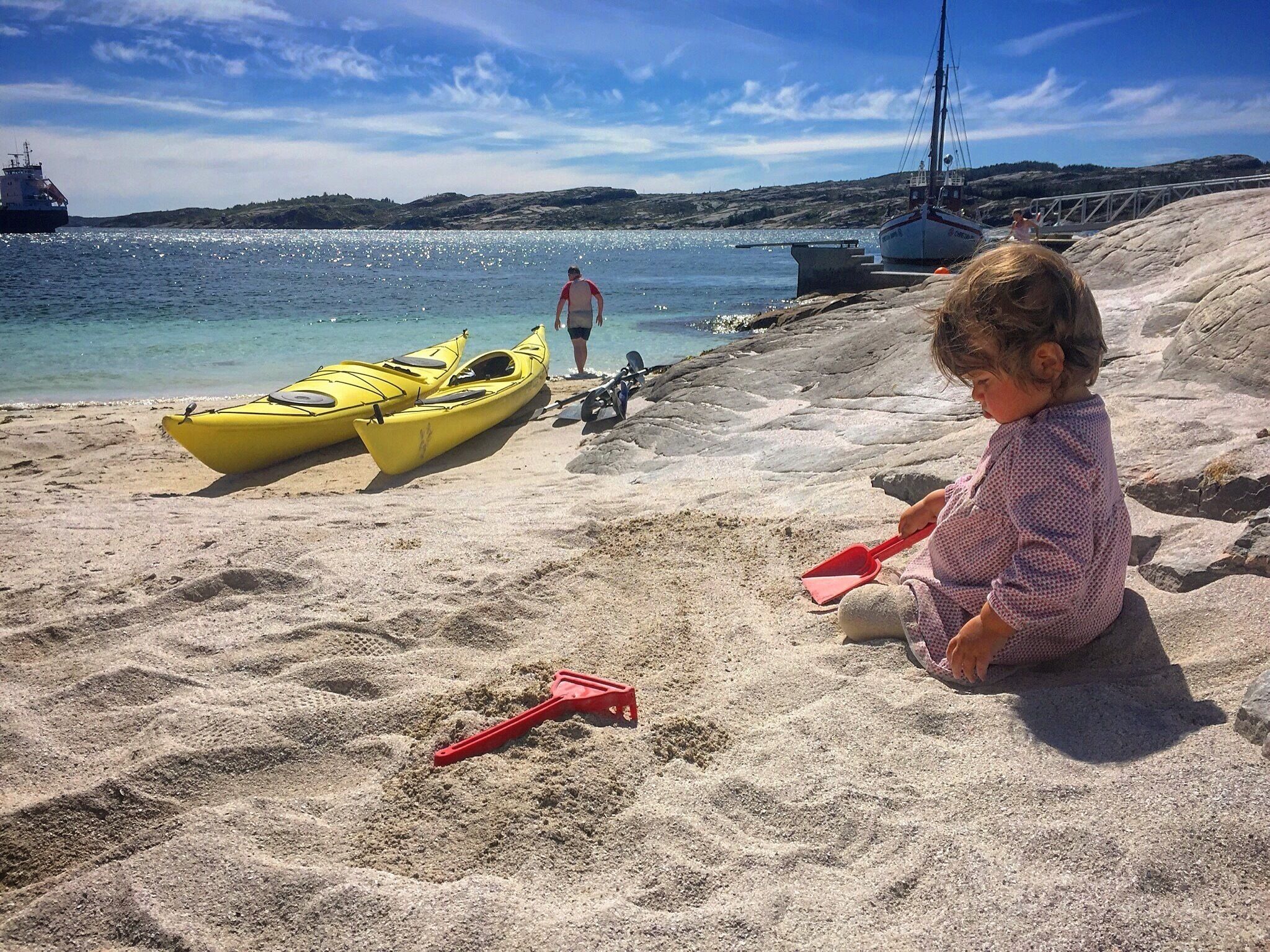 A sandy beach with kayaks and a sailboat in the background.